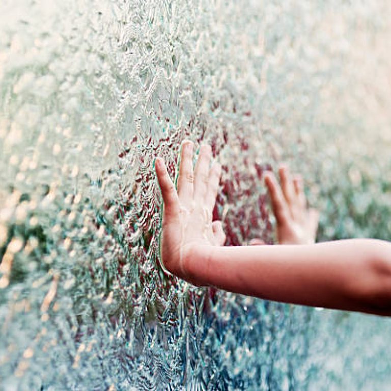 Child's hand touching water flowing on glass wall.